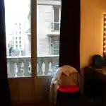 Platée - Opéra-Comique de Paris | L’intérieur élégant et intime de la loge de notre chat Ibrahaam Des Jardins Persans à l’Opéra Comique de Paris est remarquable. Le sol de la loge est recouvert d’un magnifique parquet en bois ciré. La pièce est éclairée par la lumière naturelle qui pénètre par une grande fenêtre de face, ainsi que par les lumières des miroirs sur la droite, offrant une vue imprenable sur la rue parisienne. Mon manteau repose sur une chaise rouge vif, et de lourds rideaux en velours bordeaux sont visibles en arrière-plan.