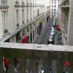 Platée - Opéra-Comique de Paris | Vue pittoresque d’une rue parisienne depuis le balcon en pierre de la loge d’Ibrahaam Des Jardins Persans, située en hauteur à l’Opéra Comique de Paris. Les bâtiments historiques, les rues pavées et l’atmosphère urbaine évoquent le charme intemporel de Paris.