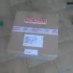 Les moments clés de l’aménagement de la chatterie | Présente un colis de livraison en carton marron. Il est muni d’étiquettes indiquant: Très fragile et Haut pour guider correctement le livreur lors de la manipulation. Le colis est posé sur un sol carrelé.