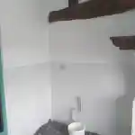 Les moments clés de l’aménagement de la chatterie | Cette image illustre la pièce de la chatterie réservée à mes chats, actuellement en cours de rénovation. Les murs sont fraîchement peints en blanc et des poutres en bois sont visibles au plafond. Un seau blanc est posé sur le sol, qui est protégé par une bâche pendant les travaux de peinture. Une installation électrique et de plomberie est prévue si nécessaire.